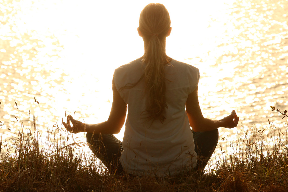 Mulher meditando na beira de um lago de dia